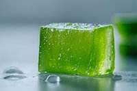 Fresh green jelly cube with water drops on light surface, macro shot showing transparent texture and moisture for food photography and dessert styling.