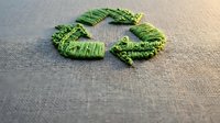 Green recycling symbol made from natural leaves arranged on textured fabric background representing eco-friendly sustainability and environmental awareness.