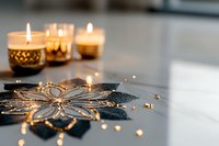 Lit candles in gold holders with decorative black snowflake and scattered gold beads on white surface, creating warm festive ambiance for holiday celebrations and seasonal home decor.