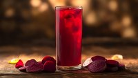 Fresh beetroot juice in tall glass with sliced beets on wooden table. Healthy detox drink for wellness and nutrition lifestyle with warm bokeh background.