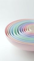 Colorful nested bowls in pastel rainbow hues arranged concentrically on white background for kitchen and dining concepts.