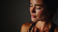 Young woman with closed eyes in dramatic lighting, face illuminated against dark background, expressing serenity and contemplation.
