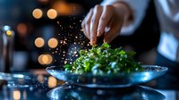 Chef garnishing fresh salad with spices and herbs in upscale restaurant setting with bokeh lights background, creating fine dining culinary experience.