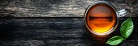 Cup of aromatic black tea with fresh green leaves on dark rustic wooden background, top view panoramic banner with copy space for text.