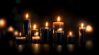 Glowing black candles with warm flames arranged in row on dark background create mystical atmospheric mood for spiritual practices and meditation.