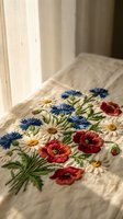 Delicate floral embroidery with daisies, cornflowers and poppies on natural linen fabric in soft sunlight for handcraft and textile design projects.