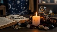 Mystical altar setup with burning candle, crystal ball, pentagram, open spell book, gemstones and occult symbols for spiritual practices and divination rituals.