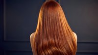 Back view of young woman with long straight red hair against dark background showcasing healthy shiny copper colored locks for beauty and haircare concepts.