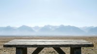 Wooden picnic table on empty desert landscape with distant mountains under clear sky, suitable for travel and nature backgrounds.