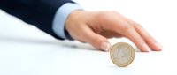 Businessman hand in dark suit and light blue shirt presenting or protecting a single pound coin on white surface, symbolizing financial security, investment, and wealth management.