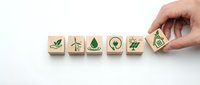 Hand placing wooden cube with dollar sign among eco-friendly symbols representing sustainable business growth and green economy investment concepts.