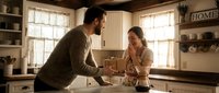 Young couple enjoying morning coffee together in cozy farmhouse kitchen with natural lighting and rustic decor elements creating intimate domestic moment.