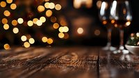 Rustic wooden table with blurred golden bokeh lights and wine glasses in background, creating romantic holiday atmosphere for festive dining and celebrations.