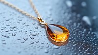 Elegant amber teardrop pendant necklace on gold chain against water droplet background creates luxurious jewelry composition with soft bokeh effect.