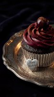 Dark chocolate cupcake with rich swirled frosting on vintage silver tray, heart charm, moody dark background for birthday celebration.