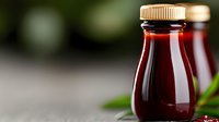 Red berry juice or syrup in glass bottle with gold cap, natural organic beverage on blurred green background.