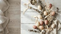 Natural Easter eggs in neutral tones with dried flowers and eucalyptus branches on white wooden background for spring holiday decoration and crafting.