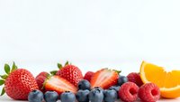 Fresh mixed berries and orange slice arranged on white background for healthy eating and nutrition concepts.