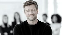 Confident Caucasian businessman with beard smiling in modern office with diverse team in background. Corporate leadership and teamwork concept for business presentations.