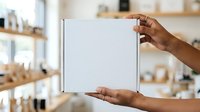 Man with dark skin tone holding blank white box in modern kitchen, product packaging mockup for branding and marketing purposes.