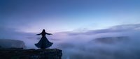 Woman in flowing dress dancing on cliff edge at twilight with misty valley below and purple sky for wellness and freedom concepts.
