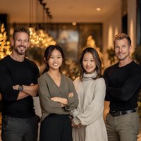 Diverse business team of four professionals standing confidently in modern office space with warm lighting and contemporary interior design.
