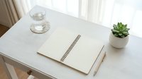Clean minimalist workspace with open notebook, coffee cup and succulent plant on white desk for productivity and planning.