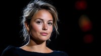 Young Caucasian woman with blonde hair in updo against dark background, soft dramatic lighting creates professional headshot mood. Natural makeup and confident expression.