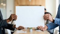 Diverse business professionals holding blank white paper sign together in modern office environment for corporate messaging and branding purposes.