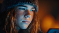 Young Caucasian woman with freckles wearing knit beanie hat in warm orange and blue lighting creating moody atmospheric portrait for lifestyle content.