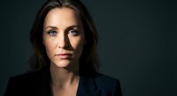 Professional portrait of confident young Caucasian businesswoman with brown hair in dark blazer against moody background for corporate headshots.