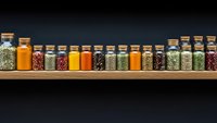 Colorful spices and herbs in glass jars arranged on wooden shelf against dark background for cooking and culinary seasoning storage organization.