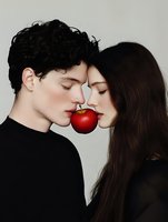 Young couple in black clothing sharing red apple with closed eyes, romantic conceptual portrait against white background. Artistic fashion photography.