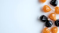 Orange and black wrapped candies on white background, perfect for Halloween seasonal designs and festive treat concepts.