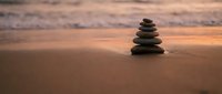 Zen stone stack on sandy beach at sunset with warm golden light and ocean waves in background creating peaceful meditation atmosphere for wellness concepts.