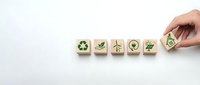 Hand placing wooden cubes with green eco symbols including recycling, checkmark, wind turbine, earth and leaf icons on white background for sustainability concept.