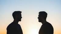 Silhouette of two men facing each other against sunset sky background, depicting confrontation, dialogue or relationship concept in dramatic lighting.