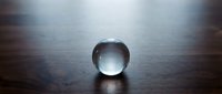 Clear glass crystal ball sphere sitting on dark wooden surface with dramatic lighting and shadows creating mystical atmosphere for fortune telling divination.