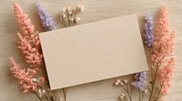 Blank beige paper card surrounded by pink and purple dried flowers on wooden background, creating romantic flat lay composition for wedding invitations.