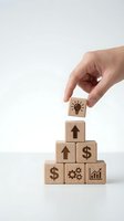 Hand placing wooden cube with lightbulb icon on pyramid of business symbol blocks representing growth strategy and innovation on white background.