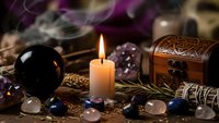 Mystical fortune telling setup with burning candle, crystal ball, amethyst gems, wooden treasure chest and sage smoke for spiritual divination practices.