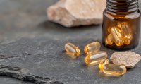 Omega-3 fish oil capsules and amber glass bottle on dark stone surface with pink salt crystals, natural supplements for health and wellness benefits.