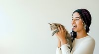 Young woman of Latin American descent holding and playing with a tabby kitten against a white background, expressing joy and affection for pets.