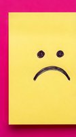 Hand-drawn sad face emoticon on yellow sticky note against bright pink background expressing negative emotions and disappointment for mental health concepts.