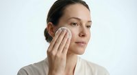 Young Caucasian woman applying skincare product with cotton pad on face during daily beauty routine for healthy glowing skin and facial care regimen.
