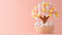 Decorative cotton ball tree in woven basket against pink background, featuring soft pastel colors of white, yellow and pink pom poms arranged as foliage.