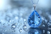 Elegant teardrop blue crystal pendant necklace with water drops on reflective surface against soft bokeh background creates luxurious jewelry composition.