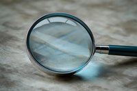 Magnifying glass with metal frame on textured surface casting soft blue reflection, closeup view showing optical distortion and investigation concept.