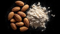 Raw almonds scattered next to pile of finely ground almond flour on dark background, overhead view of baking ingredients and healthy nuts.