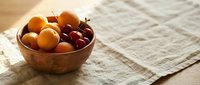 Wooden bowl filled with fresh apricots and cherries on neutral linen fabric, ideal for food styling, recipe blogs, and culinary content.